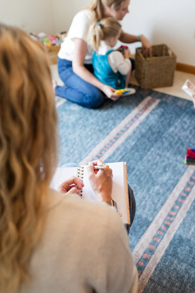 Parent coach Amy Fink writing in a notebook as she observes her client with their child