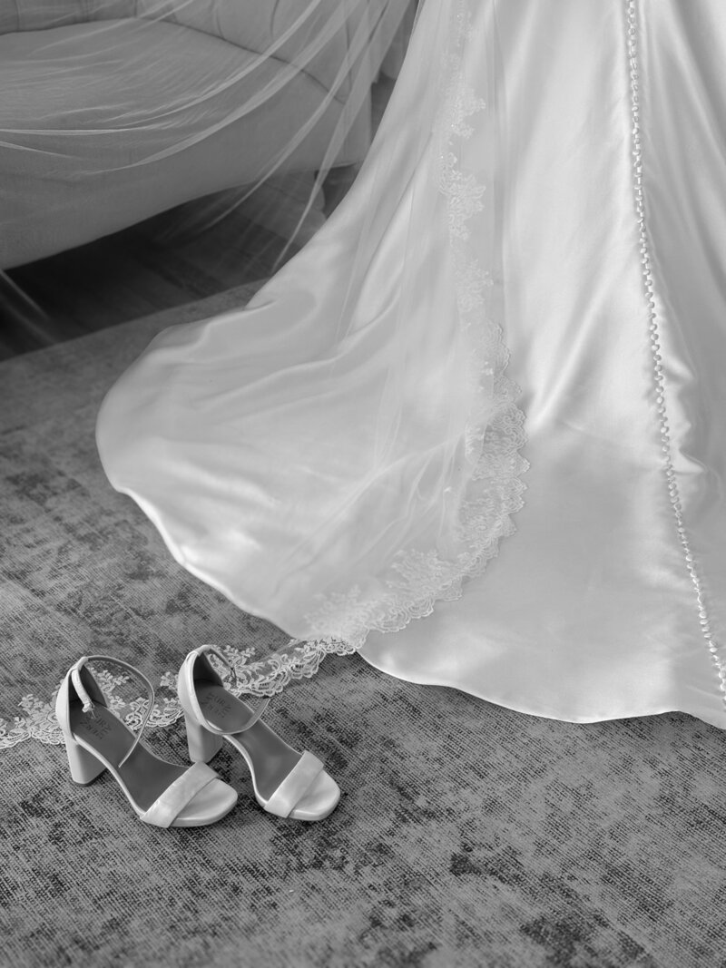 Black and white photo of a bride's dress and shoes on the floor