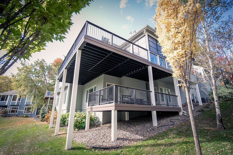 Wide view of a house with two distinct decks - one large upper and one small lower. 