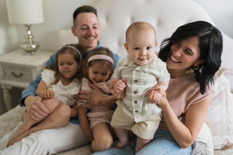 mom holding up baby with family on bed