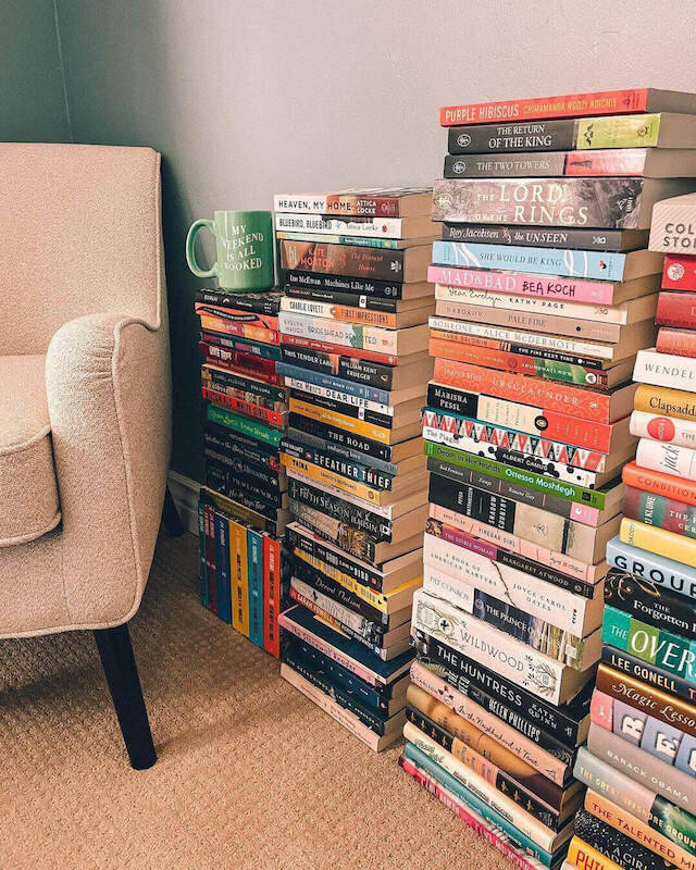 Tall stacks of books and a coffee mug next to a cozy armchair