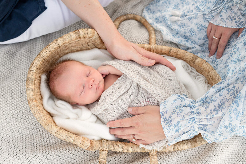 newborn baby in basket with parents hands