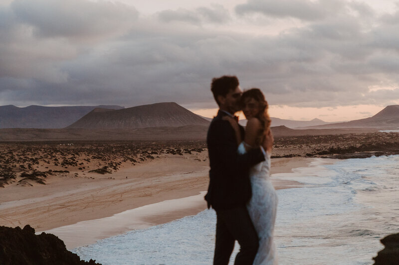 bride and groom kissing on beach cliffside