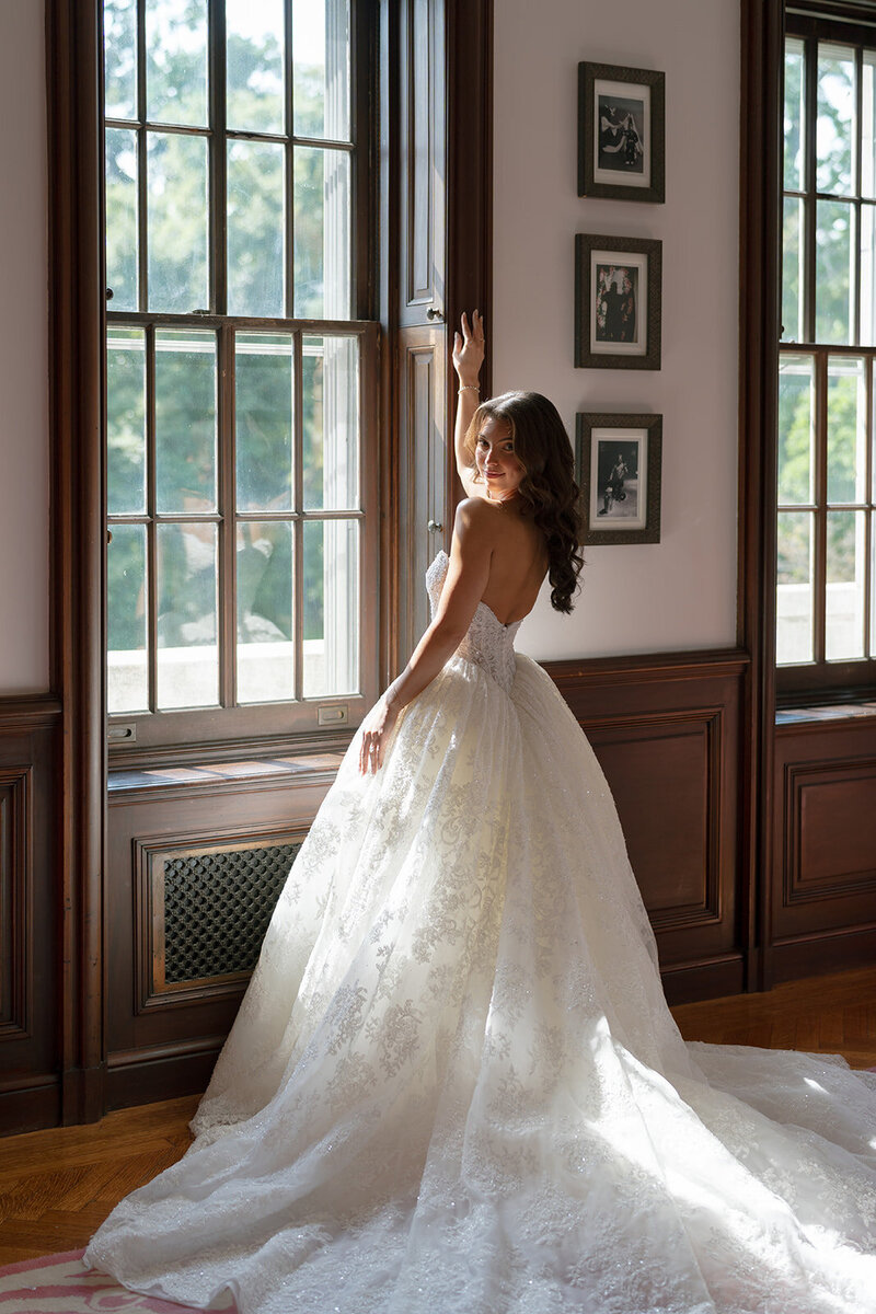 Kaitlyn in her ball gown beside a tall window at Elkins Estate