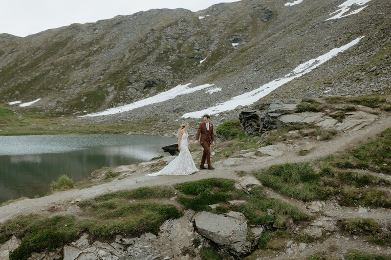 Couple holding hands and walking next to a lake.
