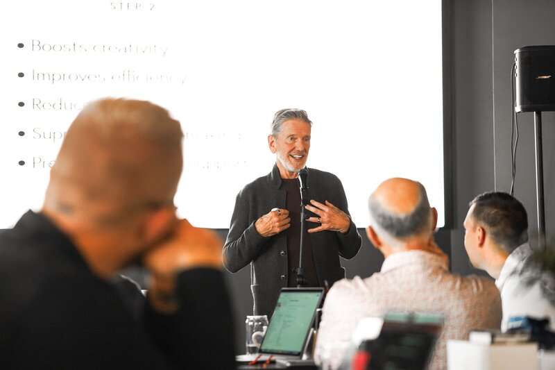 Small crowd of people seated in an auditorium, facing Michael Hyatt speaking on a stage with projected lights in the background.