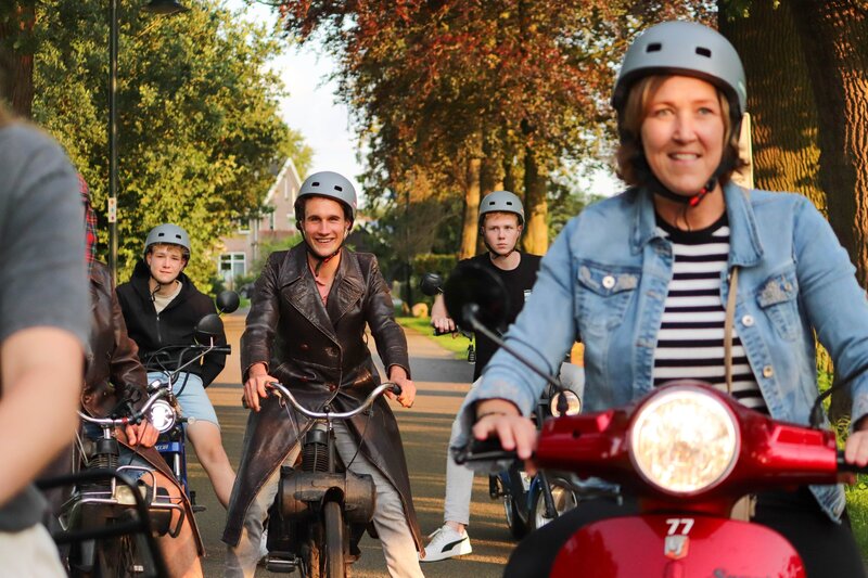 Man op een Solex tijdens een groepsactiviteit, naast het hoofdmenu van de website.