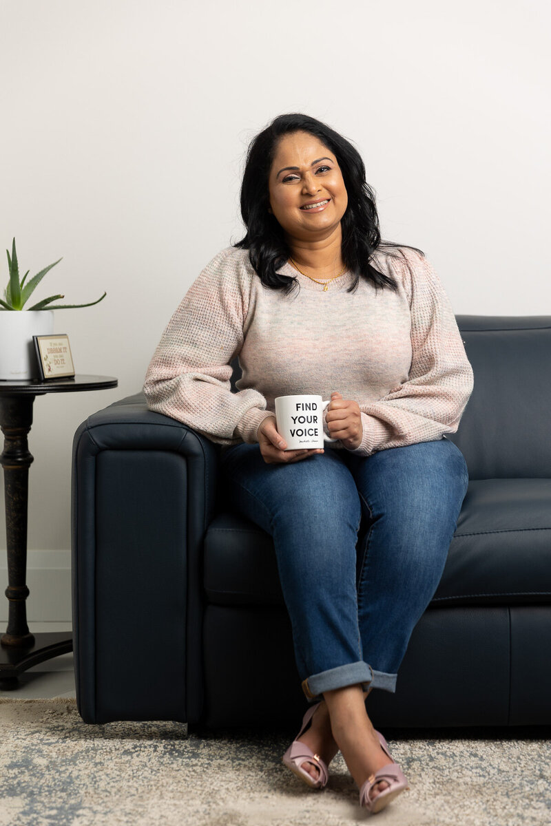 Kalinie sitting on a couch with a mug that reads "find your voice."