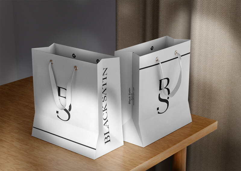 Two elegant shopping bags with "BLACKSAIN" branding on a wooden shelf.