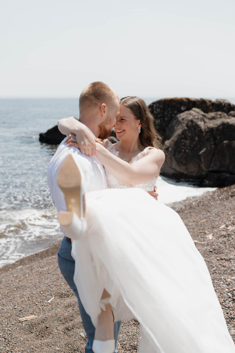 A person holding up their partner as they smile at each other on the beach 