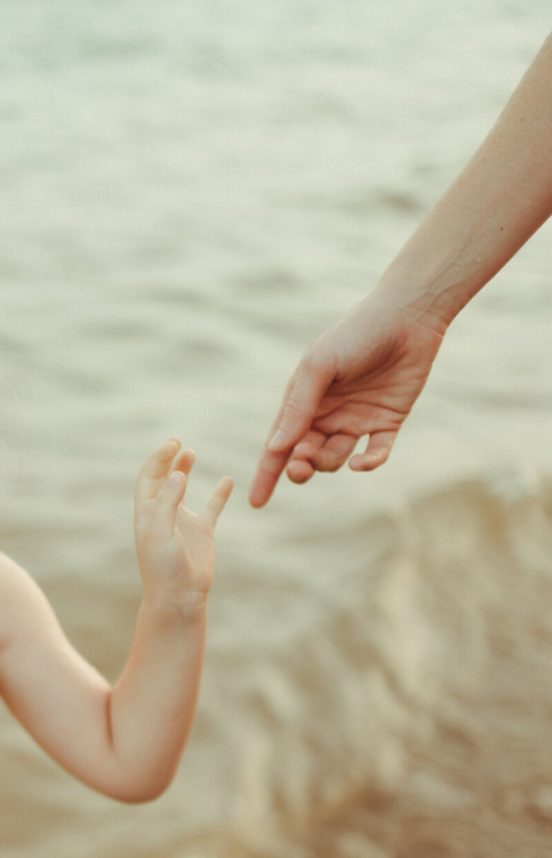 Mother's hand reaching for her toddler's hand.
