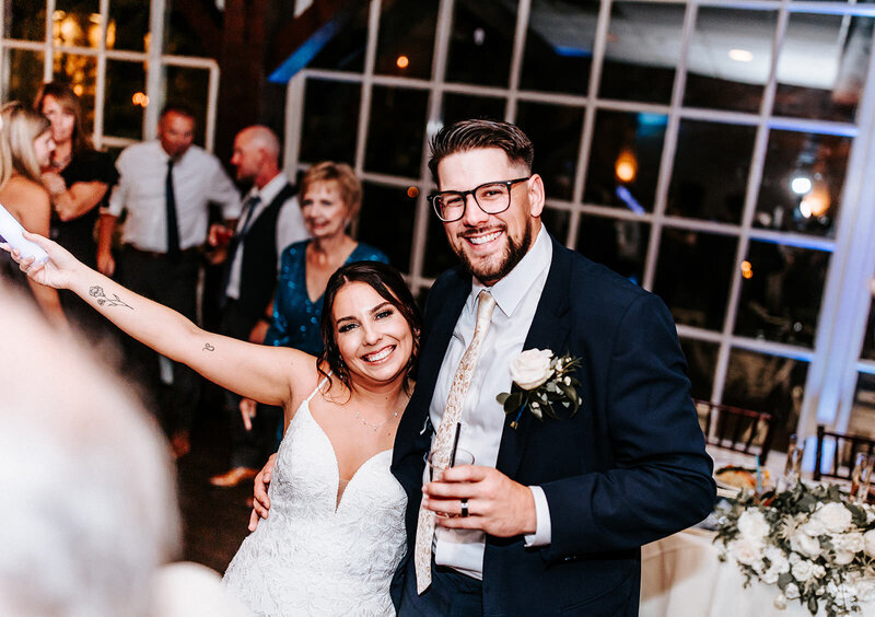 Bride and groom happily smiling together at their wedding reception while groom holds a drink and bride holds a light wand.