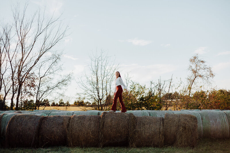 Senior walking on hay bales looking behind her during a senior portrait in De Soto, Missouri. 