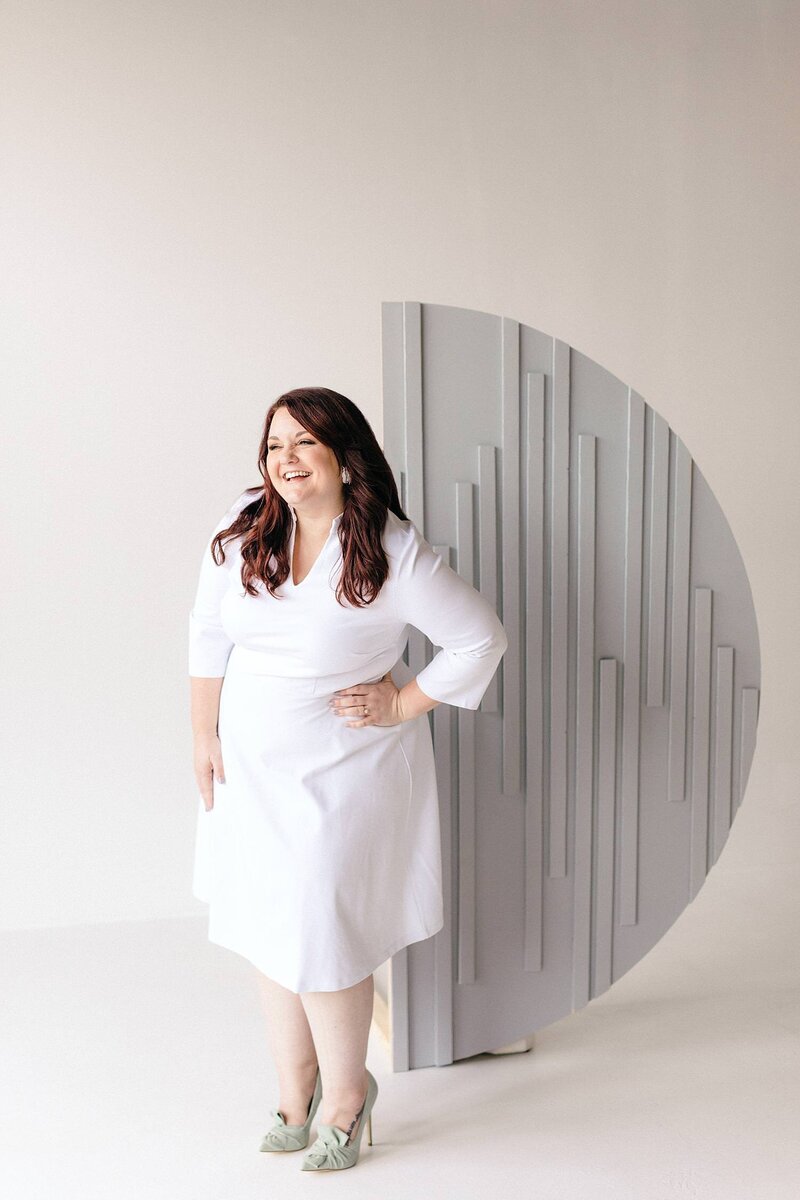 Photographer and educator, Emily, smiles in white dress and heels