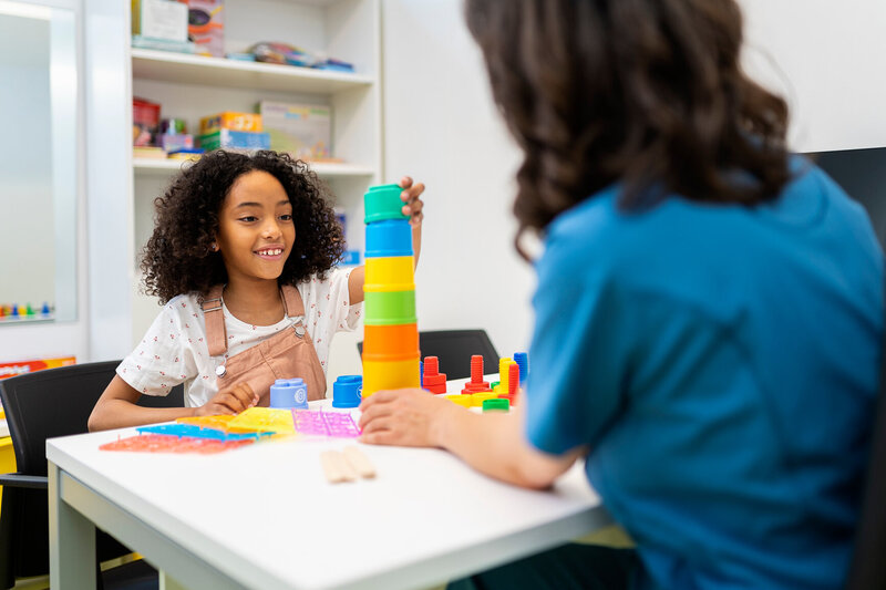 Happy adolescent girl stacking cups with psychologist