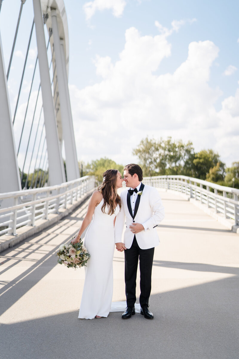 Bride and groom smile and nuzzle each other as they walk across the Main Street Bridge in downtown Columbus Ohio