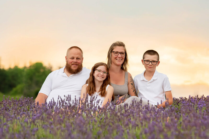 Woman wearing a blue and white dress sitting with her husband on the ground holding her baby belly in a lavender field for her outdoor Burlington Maternity Photography session.