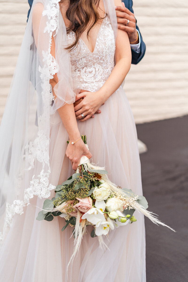 close up details of wedding couple embracing showing the flowers and wedding bands