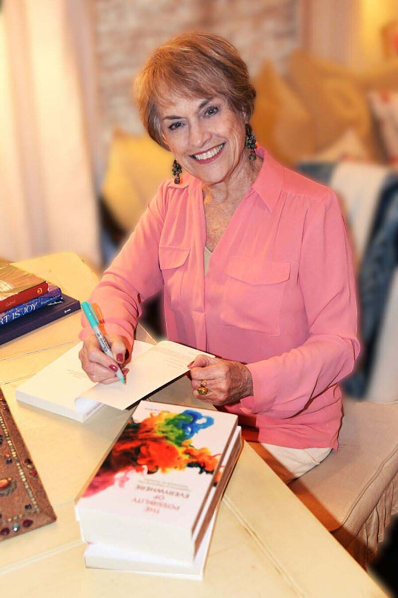 Beth Harkins, author in a pink shirt autographing her book, The Possibility or Everywhere.