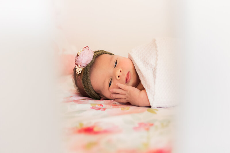 baby peeking through crib with floral sheet