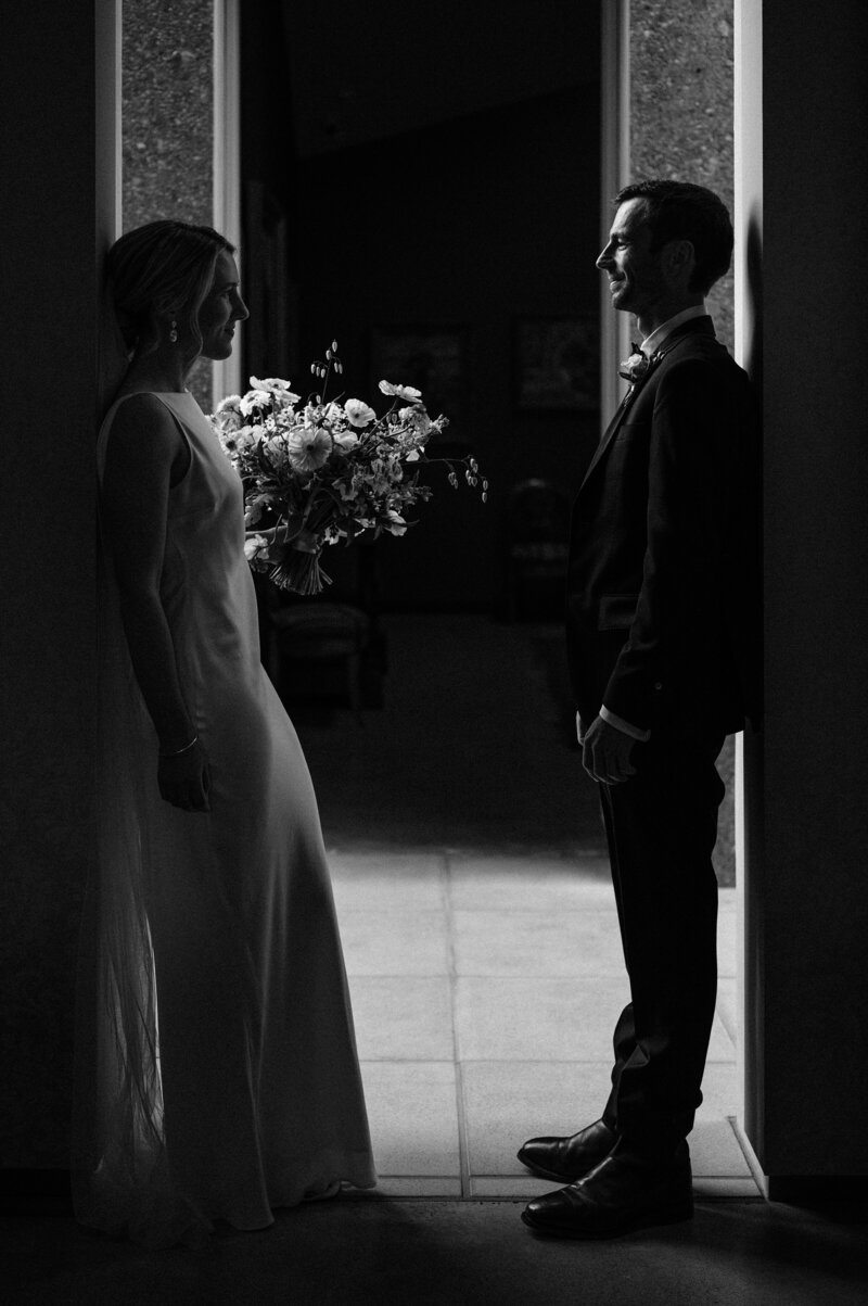 a black and white photo of a bride and groom holding bouquet silhouetted against a concrete wall