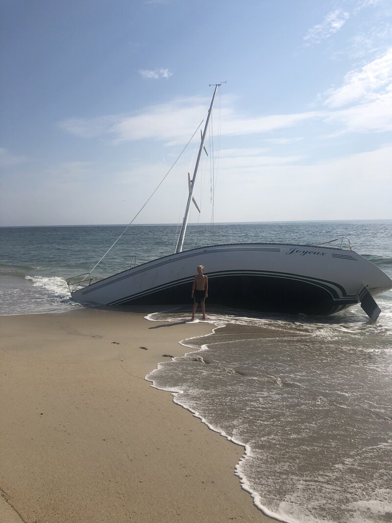blonde hair boy standing in front of capsized boat on beach in Sea Bright, NJ