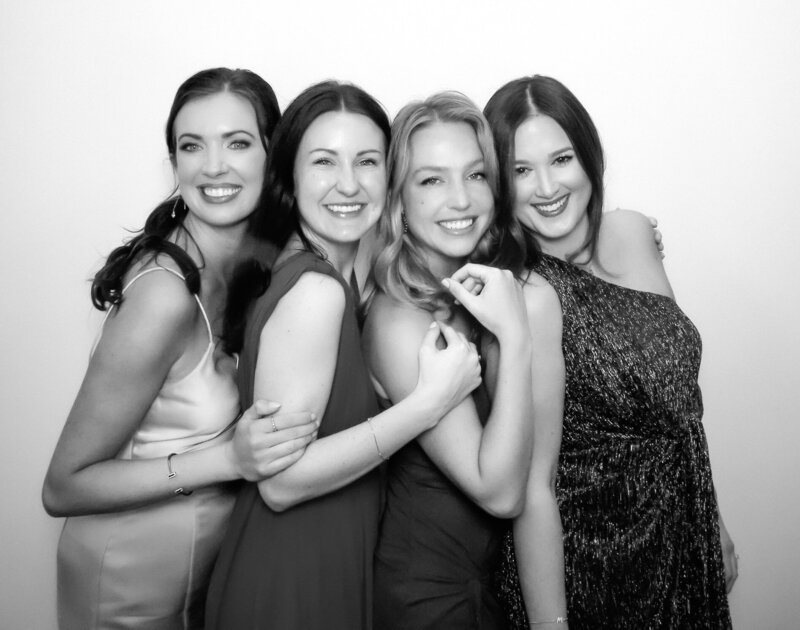 black and white image of 4 women in formal dresses in a Heirloom Glam Photo Booth during a wedding reception