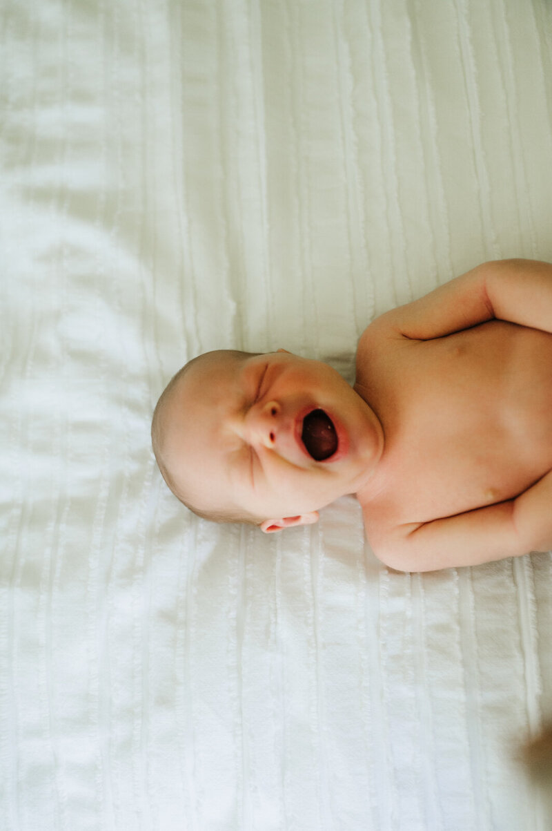 baby laying on a bed yawning for a boston newborn session