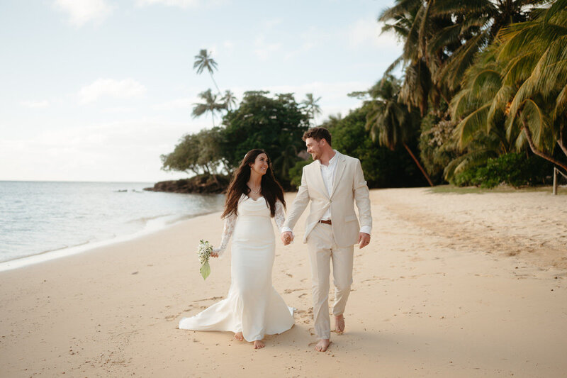 Elopement Photo Ideas | Eloping couple walk down the beach in Fiji smiling at each other