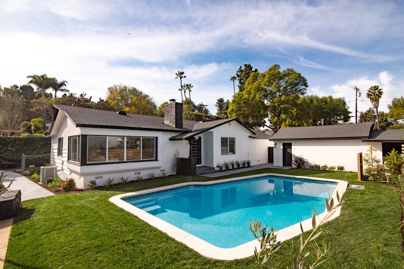 Backyard view of a renovated ranch-style home in Los Angeles with white stucco exterior, black trim, and a modern in-ground pool—designed and built by AW Development Co.