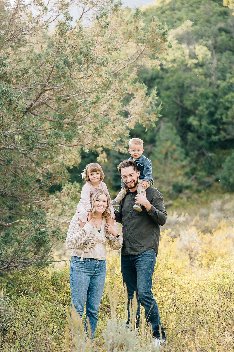 Young toddler boy is on dads shoulders and looking at mom as she looks up to him and laughs.