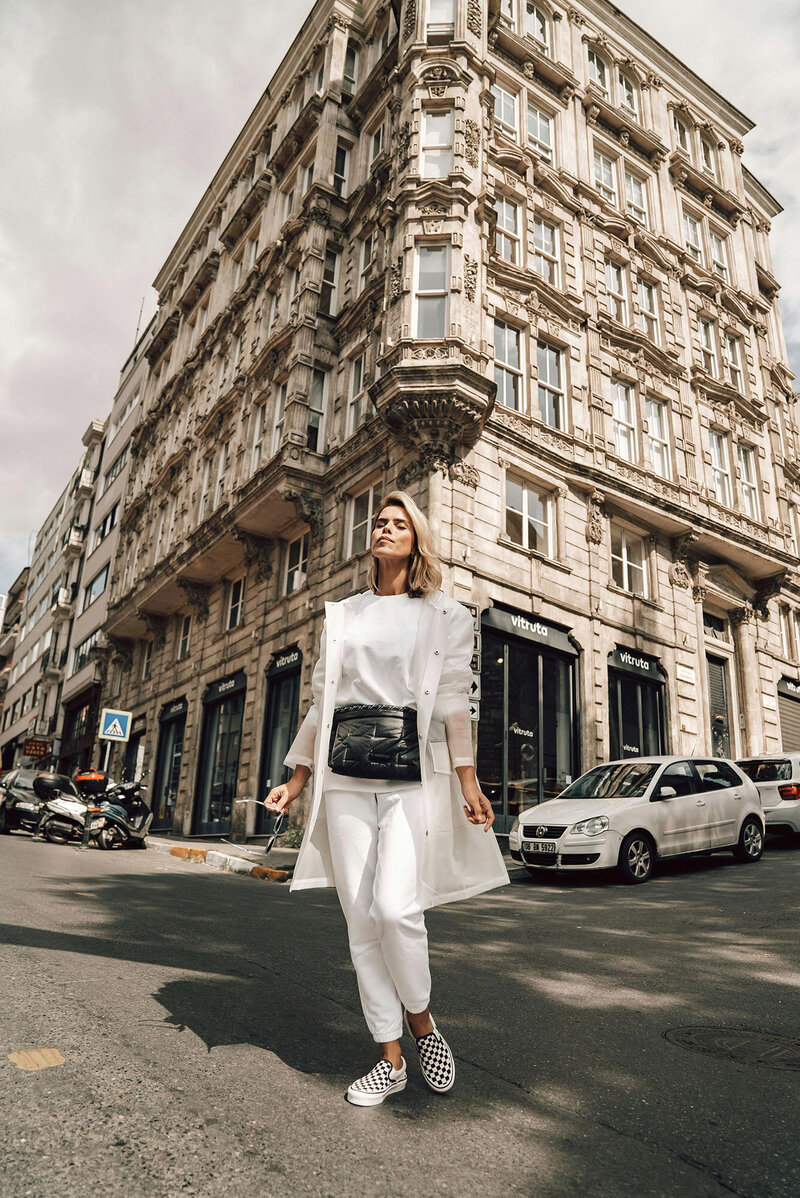 Confident woman in a crisp white outfit in an urban setting, with an art deco building in the background, lifting her face to the light as she enjoys financial well-being. Kim Russell’s journey is proof that financial success and work-life balance go hand in hand—helping business owners create sustainable financial health and freedom.