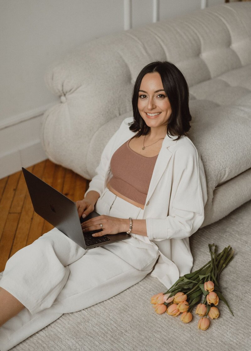 Vickie Chountalos of VERVE & COLOR leaning on a sofa with a laptop on her lap, tulips placed beside her.