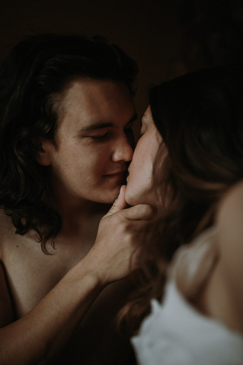 A wedding couple kissing in bed in moody lighting. The groom is shirtless.