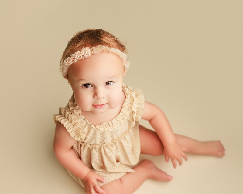 Smiling baby on mustard yellow backdrop during fun milestone session