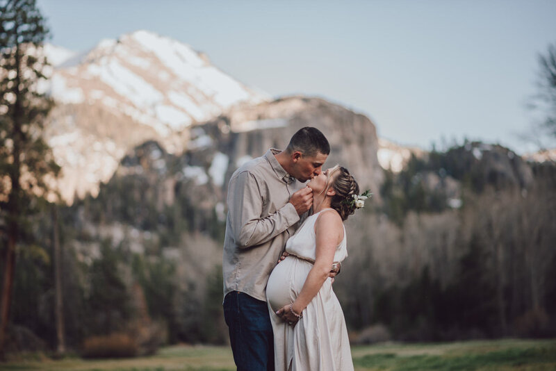 pregnant woman kissing her husband in front of a snow capped mountain