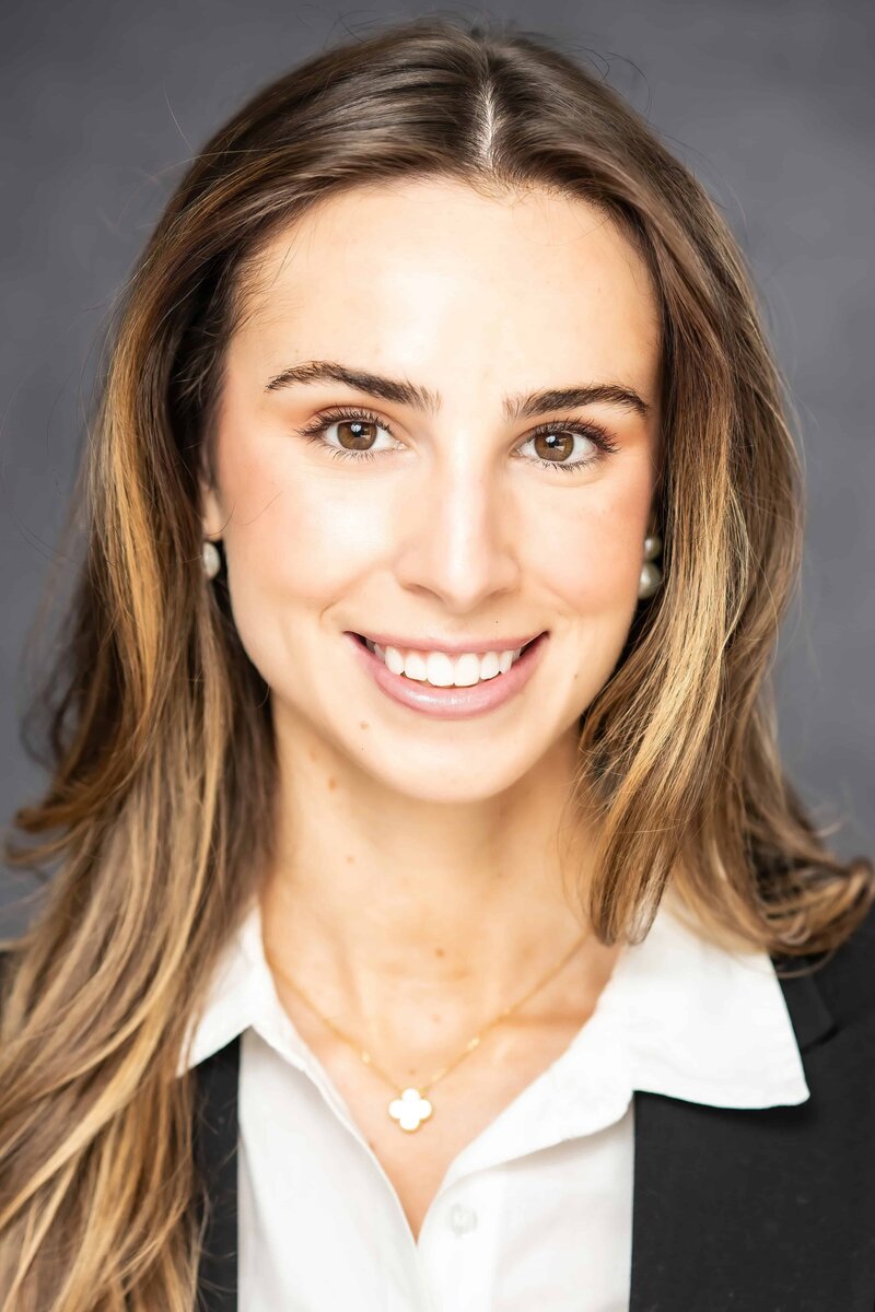 Professional headshot of a smiling woman with long hair in San Francisco wearing a dark jacket, white blouse, and a gold chain with a pendant 