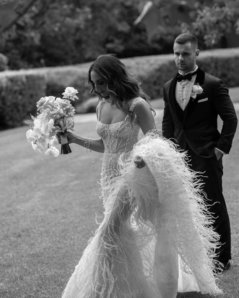 Bride holding bouquet with groom in black tux behind her