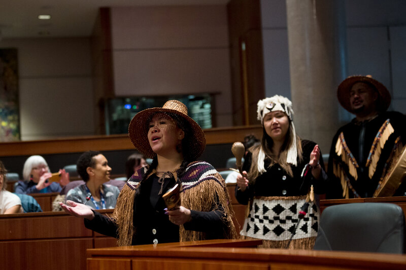 Two women in traditional woven clothing singing and playing instruments.