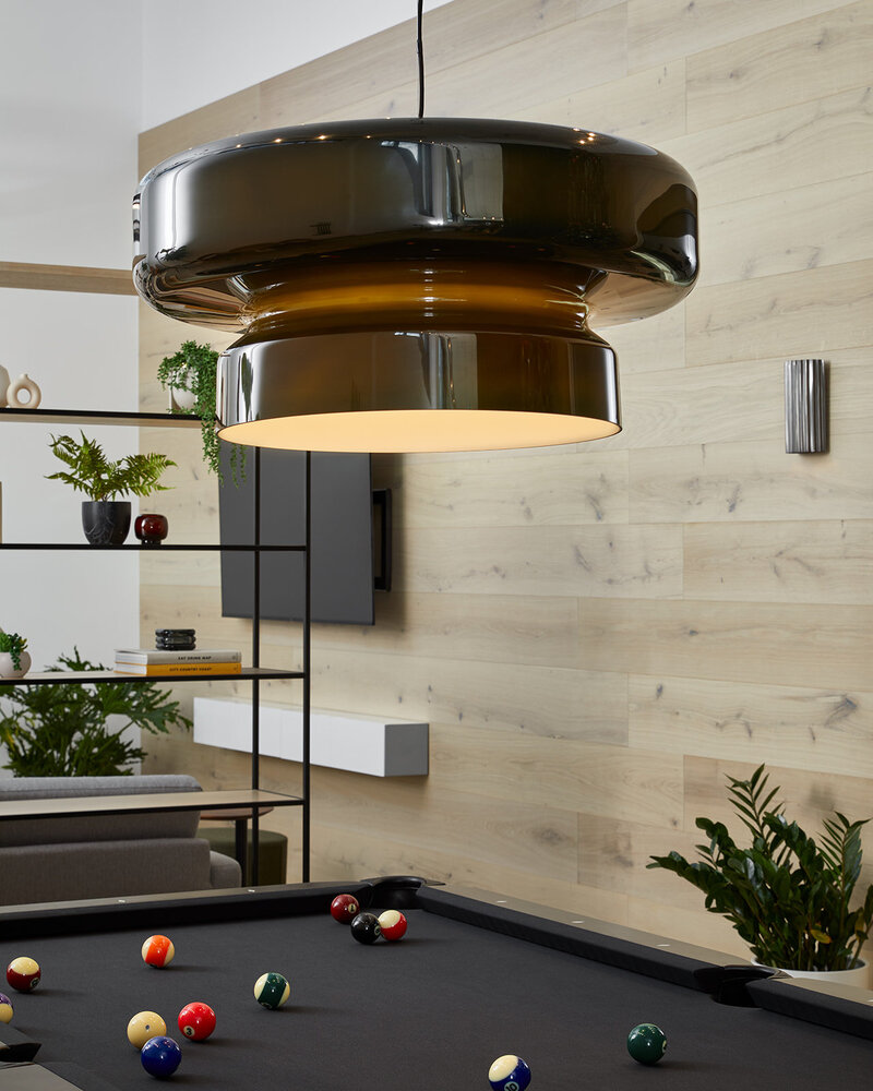 An indoor lounge space equipped with a foosball table, open shelves, large TV screen, decorative plants, and a large circular lighting fixture