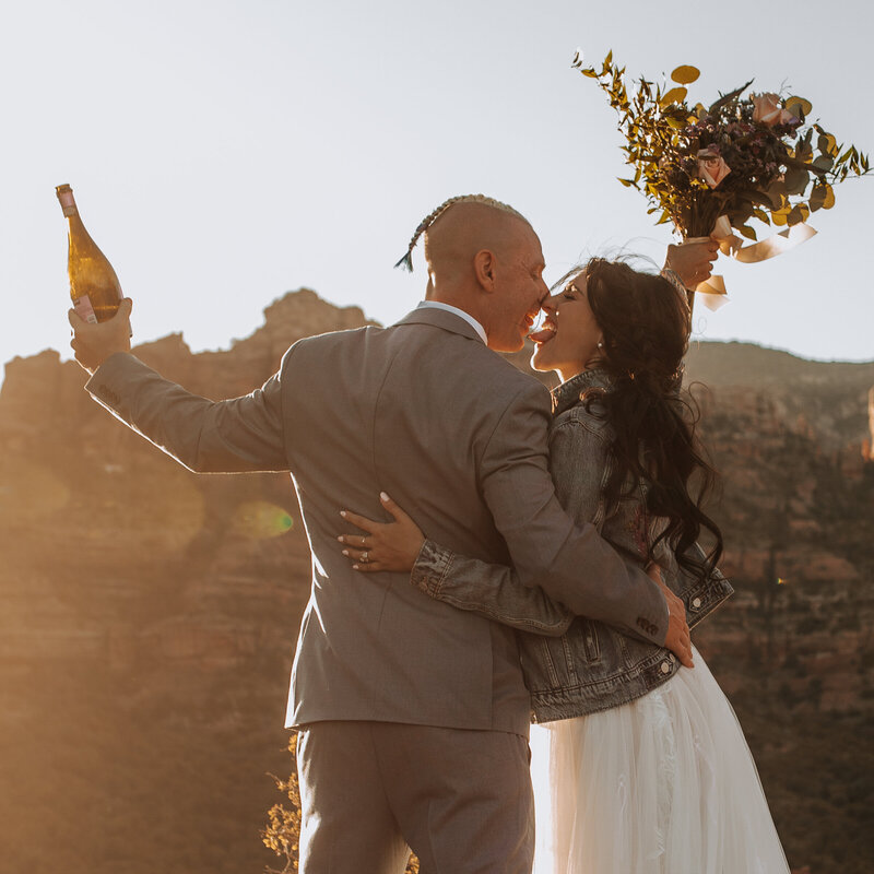 goofy bride and groom with bouquet in the air and champagne at sedona elopement