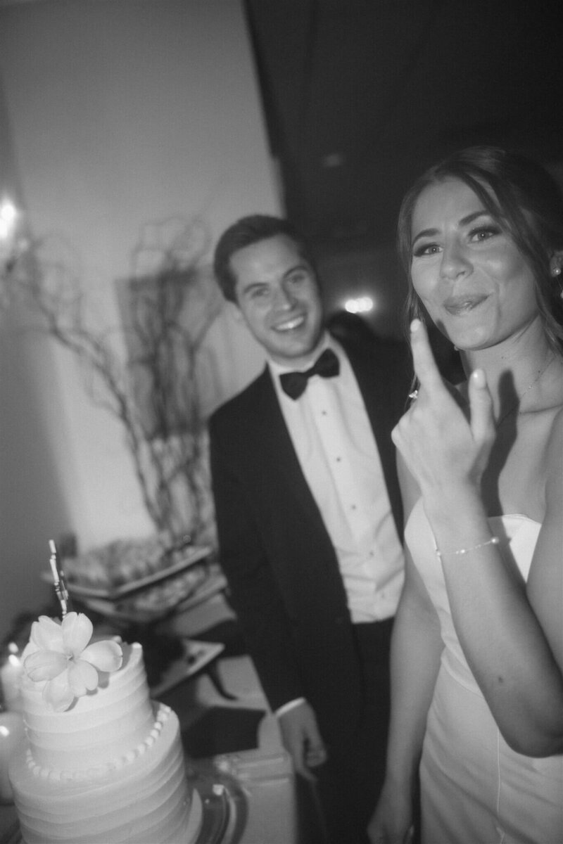 Bride licks her finger after dipping it in her wedding cake as groom smiles on