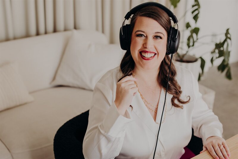 woman speaking smiling in front of podcast yeti mic in white shirt and headphone