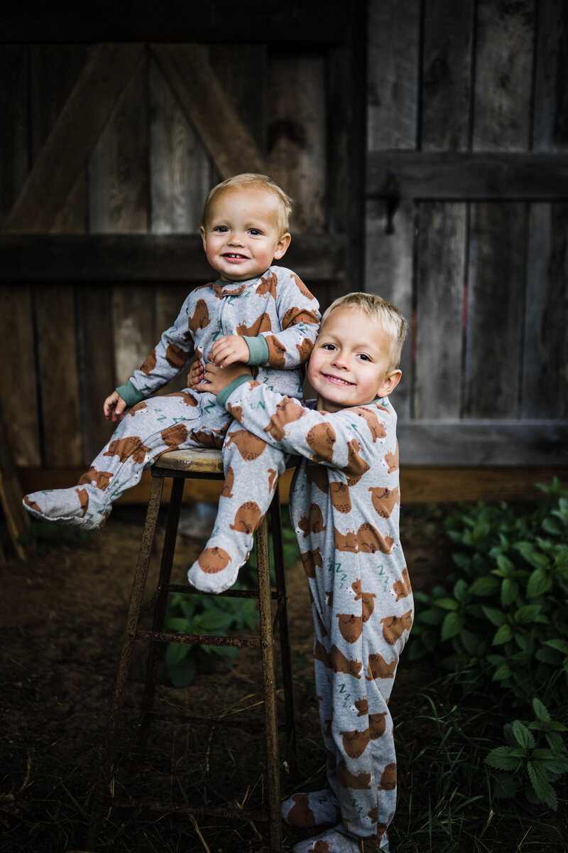 Two young brothers in teddy bear pajamas hugging outside.