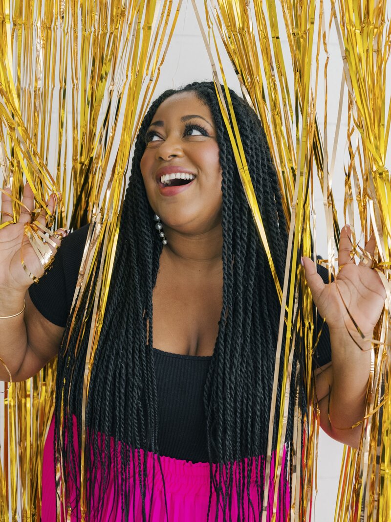 Woman standing inside gold fringe backdrop smiling and looking away from the camera