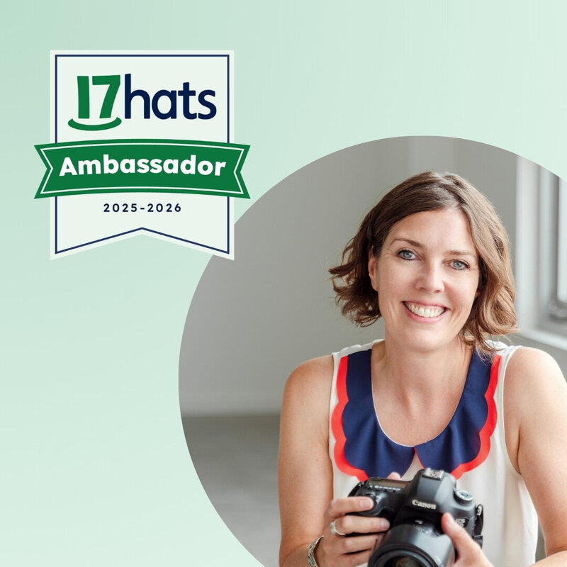 Calgary Brand Photographer Kate Daniel Photography in a white shirt and holding her camera while sitting in a chair. There is a 17hats 2024-2025 Ambassador graphic on the image, with green arrows.