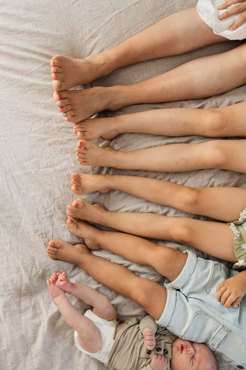 A creative lifestyle shot of a newborn baby alongside their siblings, showcasing tender family connections. Captured by Cleveland's premier lifestyle newborn photographer.