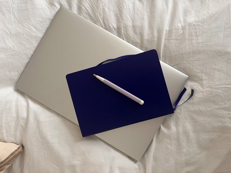 blue laptop on top of notebook on bed