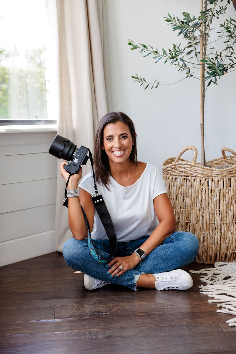 woman sitting with her camera in her hand and smiling for brand photo in a studio space captured by Orlando photographer
