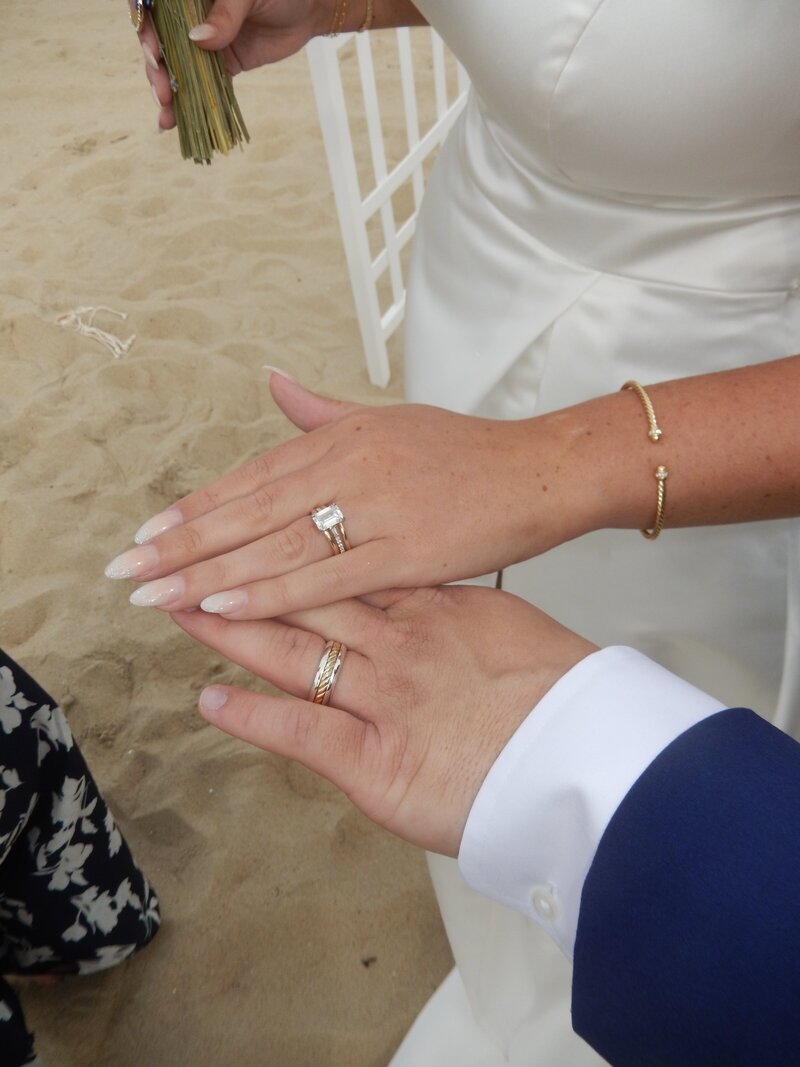 A bride's hand resting on top of her groom's hand to show off their wedding bands